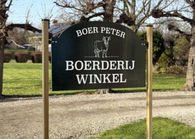 Groen reclamebord op houten palen voor een boerderij in een landelijke omgeving